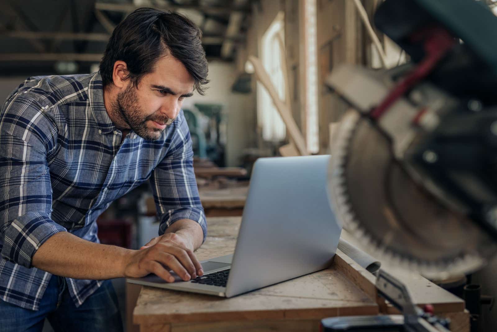 Business man working on his laptop in his joinery workshop.